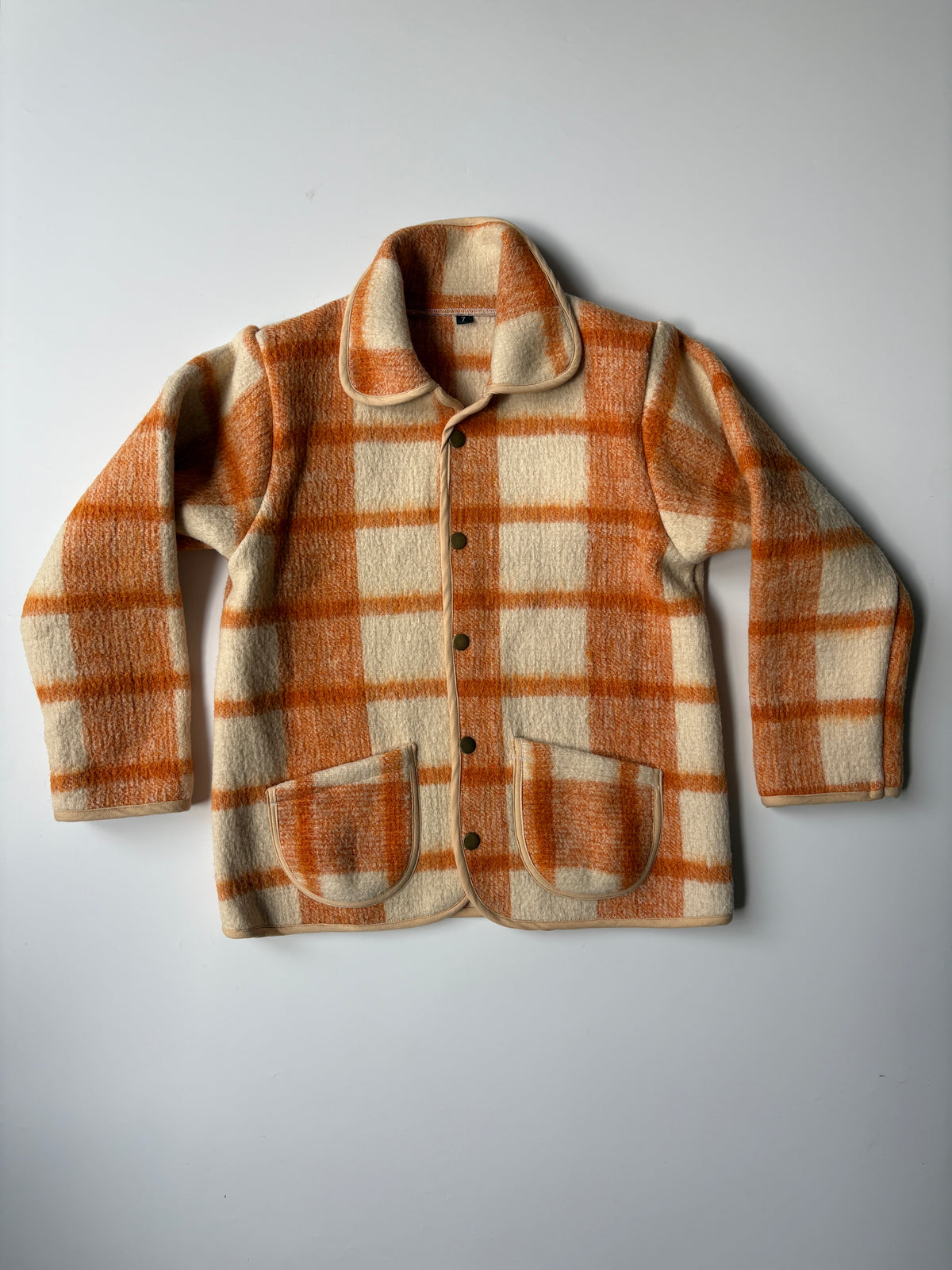Cream and orange plaid blanket children's jacket. A children's button-front jacket with a warm orange and cream plaid pattern, laid flat on a light gray background.
