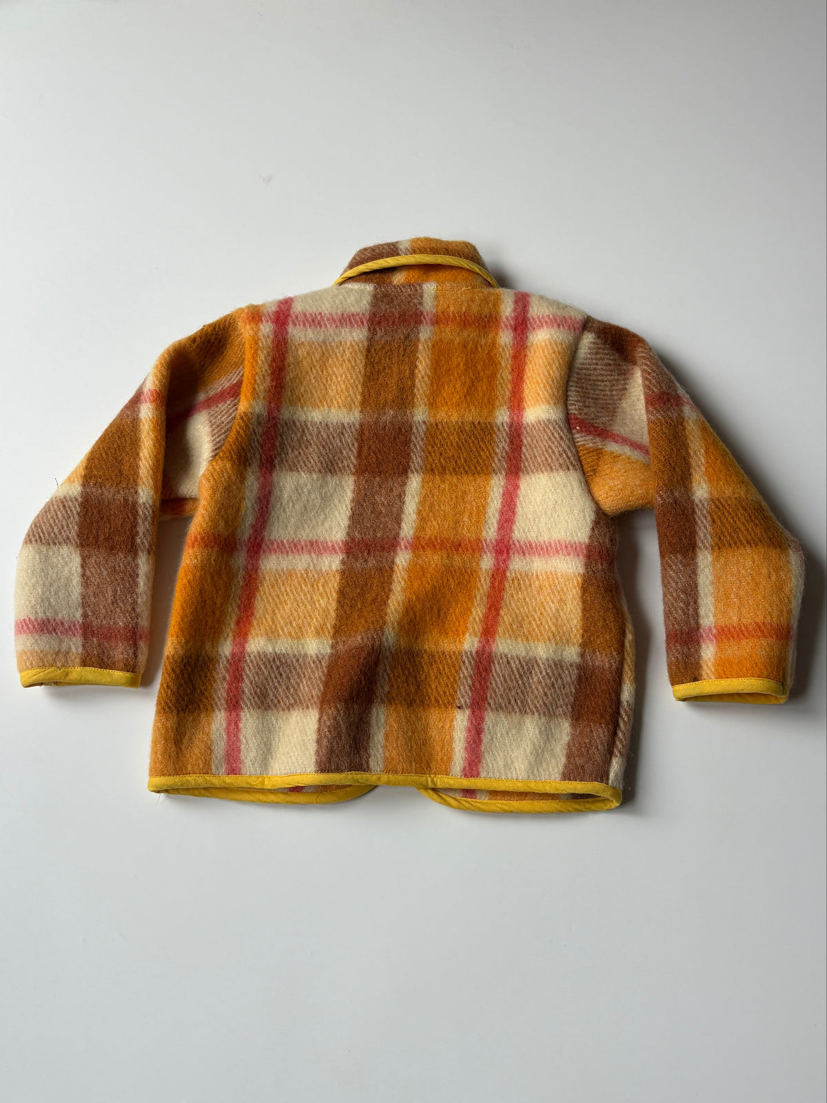 Orange, brown, and cream plaid children's jacket with yellow trim, laid flat on a light gray background.