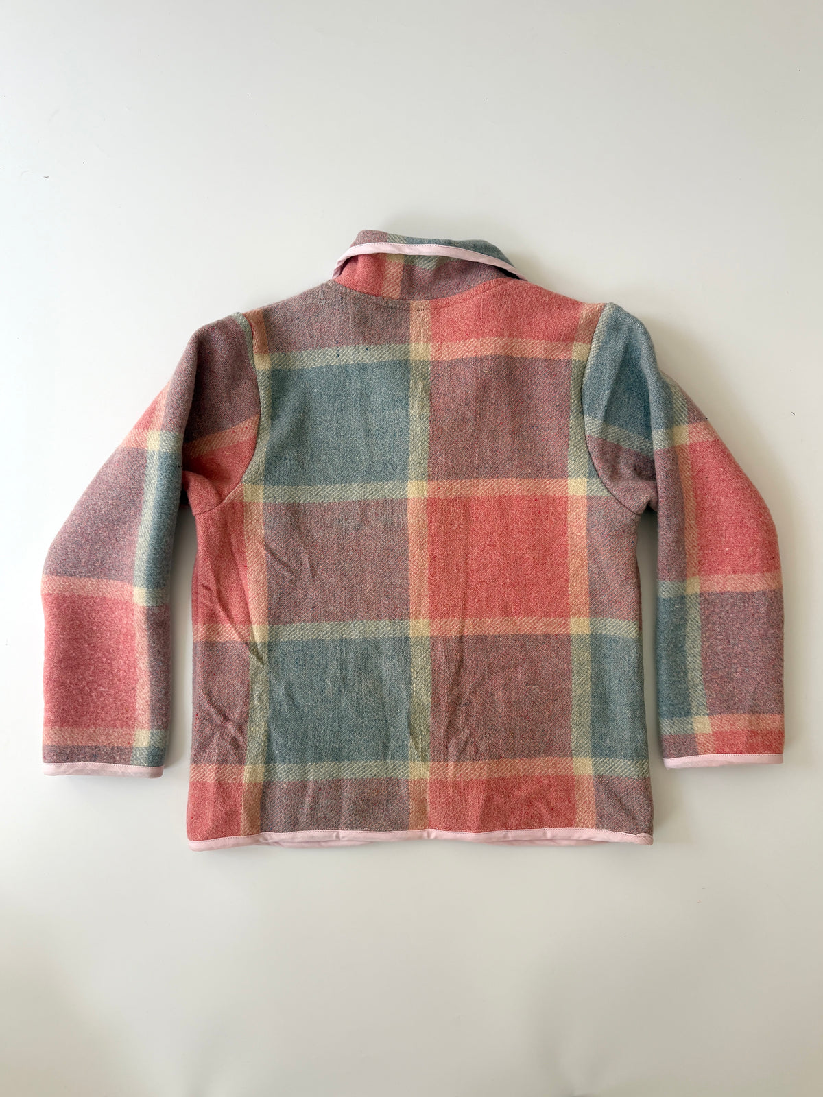 A children's long-sleeve jacket with a pink, blue, and beige plaid pattern, featuring a Peter Pan collar, button front, and two front patch pockets, laid flat against a light background.