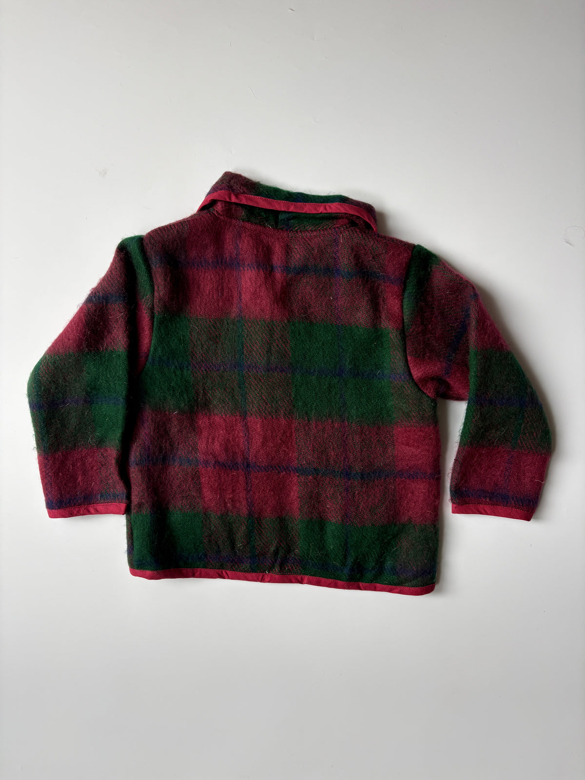Red and green plaid blanket children's jacket, featuring a collar, button front, and two front pockets, laid flat against a light gray background.