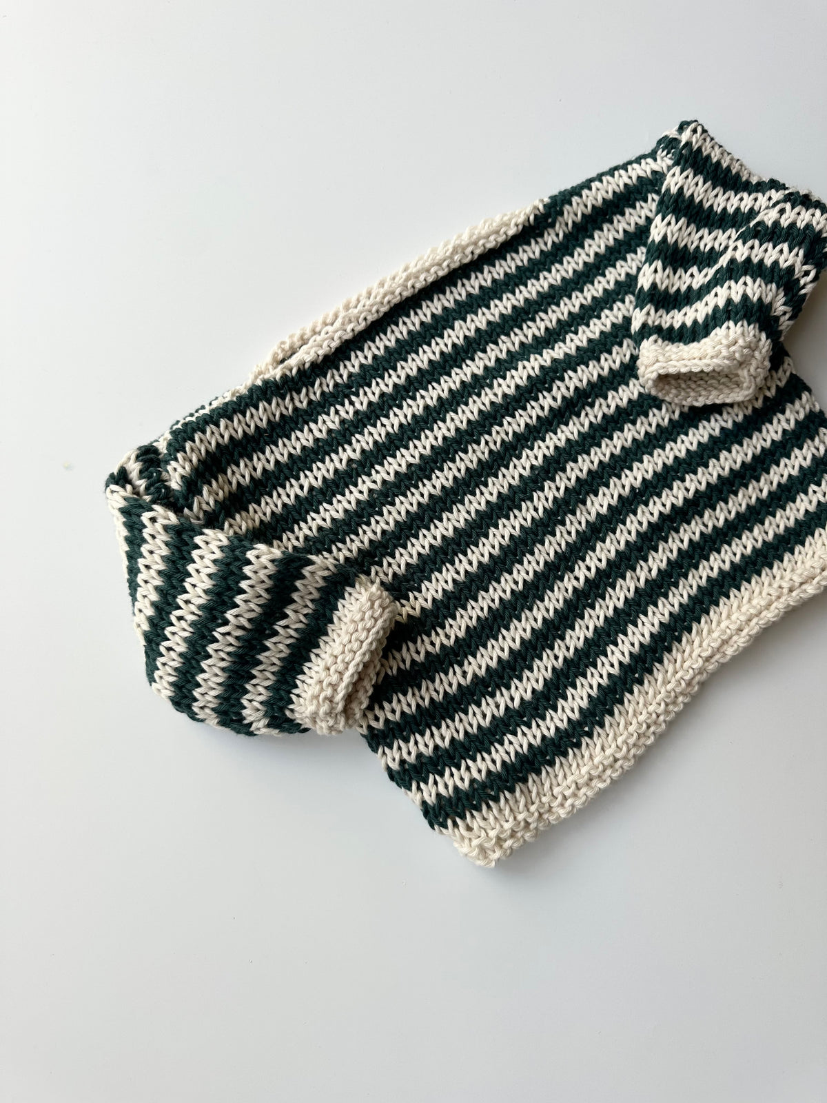 A hand-knit children's jumper in alternating blue and white colors, laid flat on a light gray background.