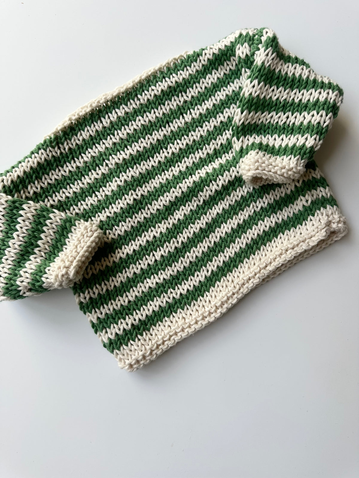 A hand-knit striped sweater in green and cream, lying flat on a light gray background.