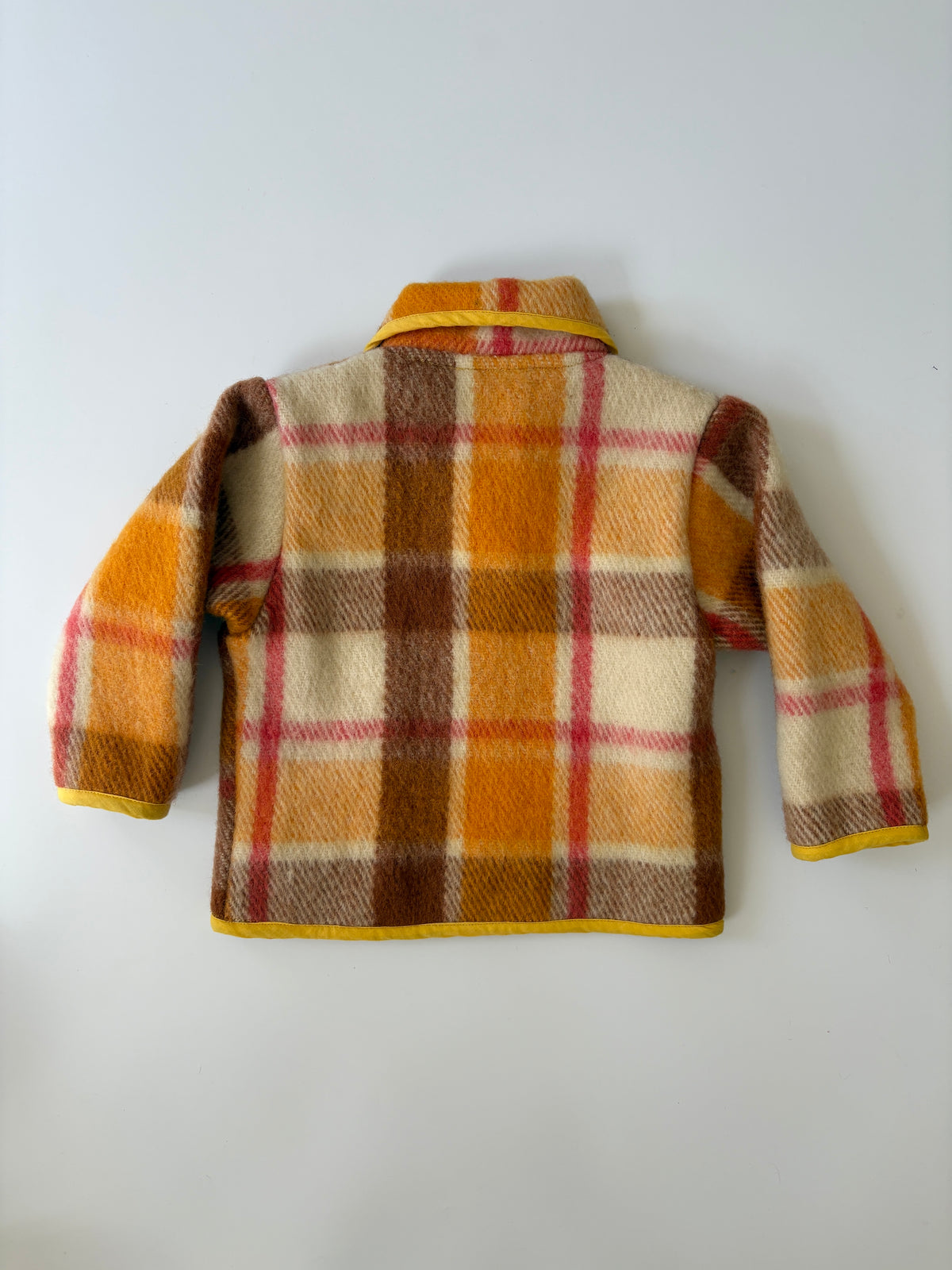 Upcycled children's plaid jacket in orange, brown, and cream, featuring a yellow collar, trim, and pocket edges, laid flat against a light gray background.