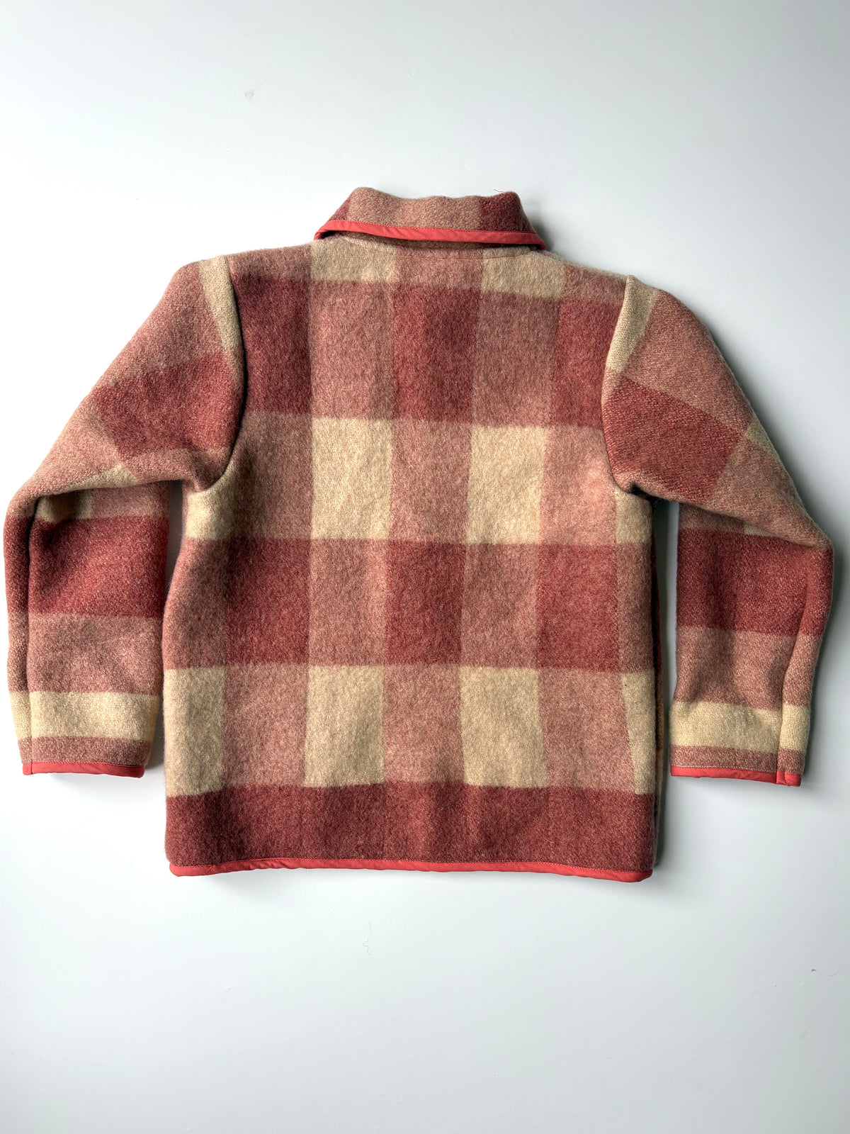 A red and cream plaid blanket children's jacket, featuring a Peter Pan collar, button closure, and two front patch pockets with red piping, laid flat against a light gray background.