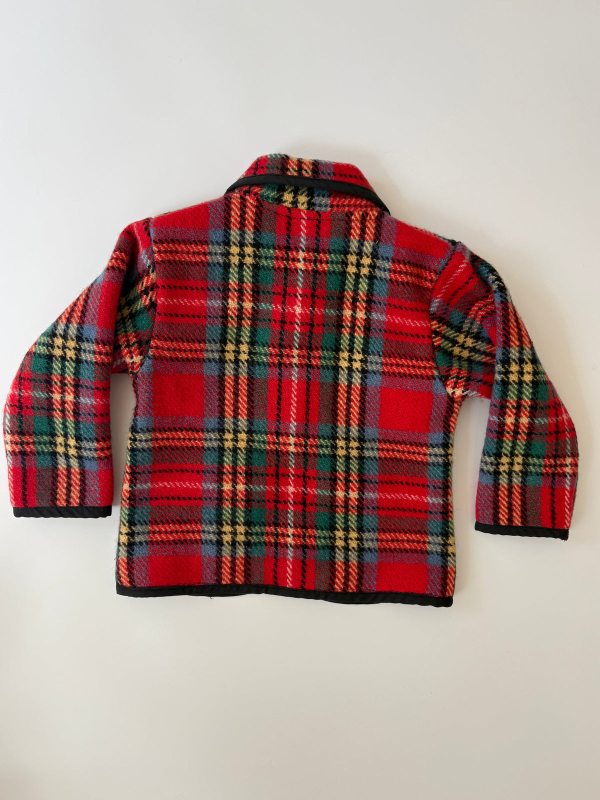 A red and green tartan plaid children's jacket with black trim, a collar, and front buttons, laid flat against a light background.