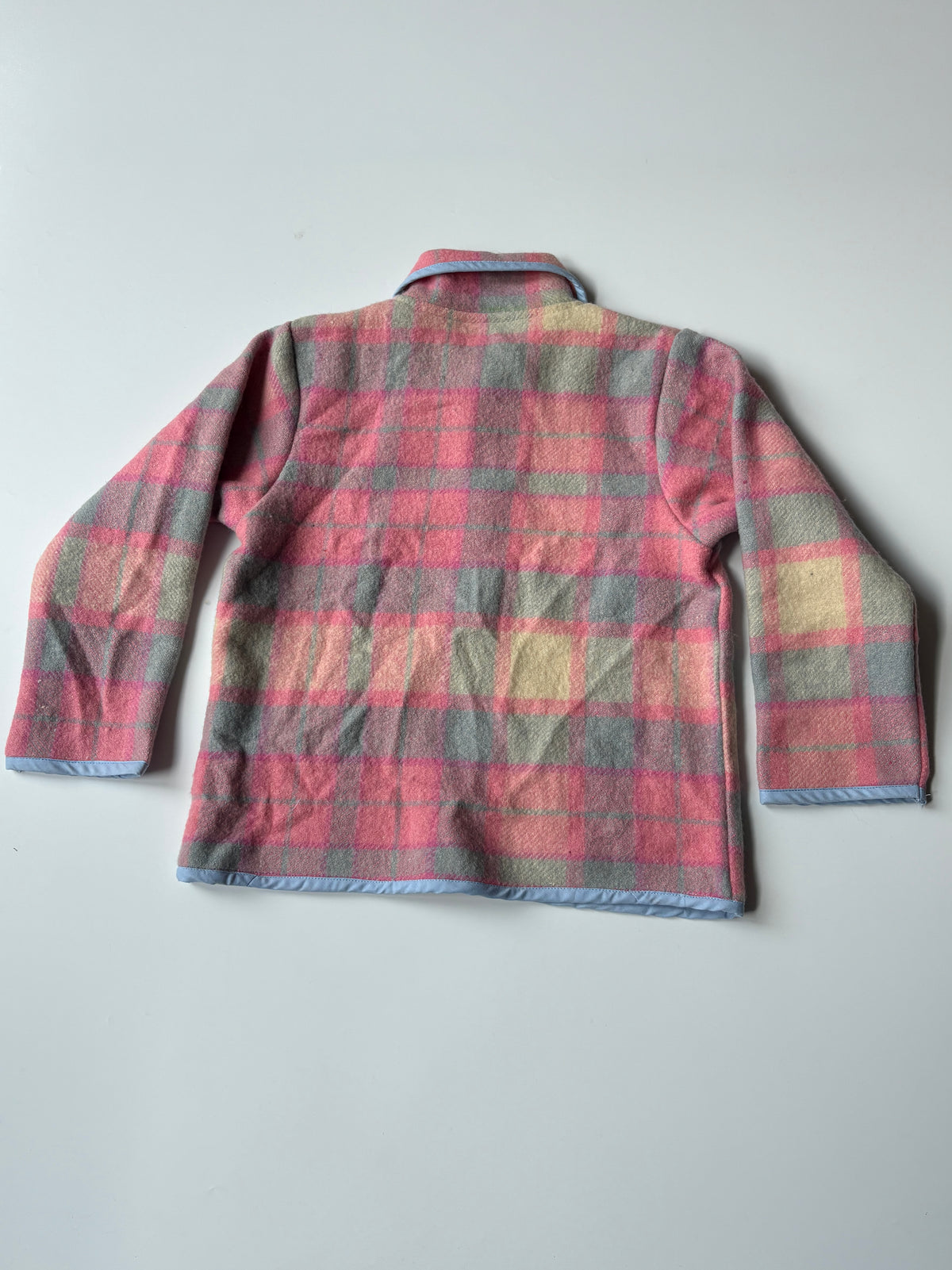 A long-sleeve plaid fleece jacket shown from the back, featuring a pink, blue, and beige checkered pattern with light blue trim on the collar, cuffs, and hem, laid flat on a light gray background.