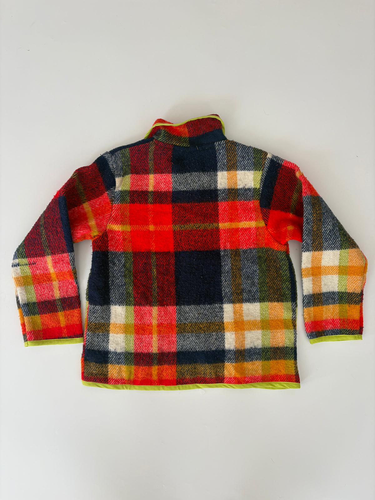 A long-sleeve plaid jacket shown from the back, featuring a vibrant red, navy blue, yellow, and white checkered pattern with a lime green inner lining visible at the collar and cuffs, laid flat against a light gray background.