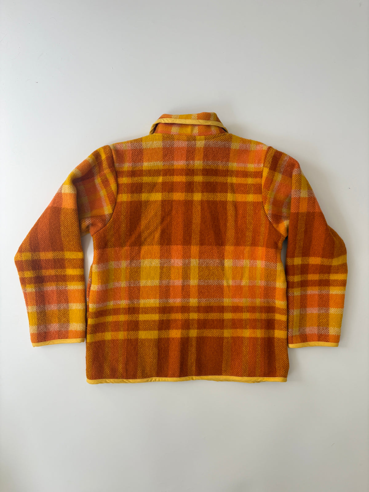 Orange and yellow plaid blanket children's jacket, featuring a Peter Pan collar, yellow piping, and two front patch pockets, laid flat on a white background.