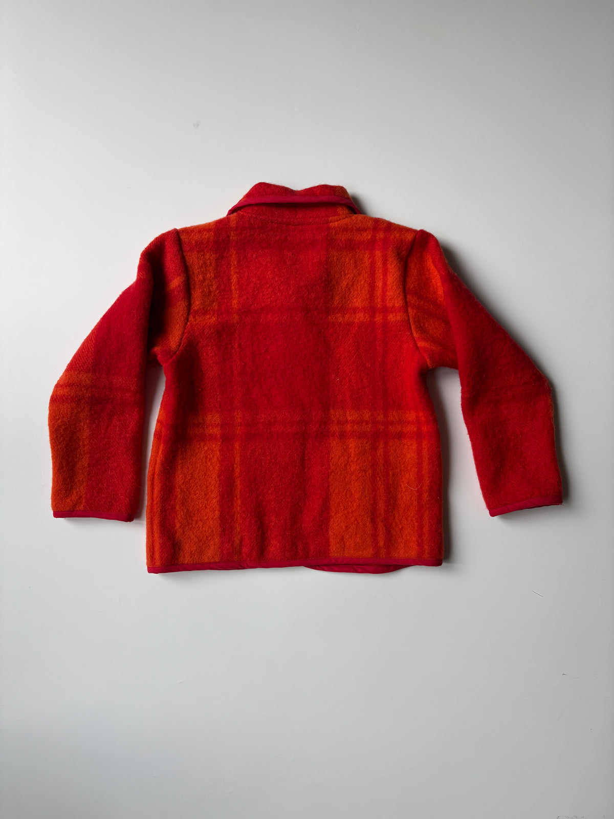 Orange & red plaid blanket children's jacket with a button front and two front patch pockets, laid flat on a light gray background.