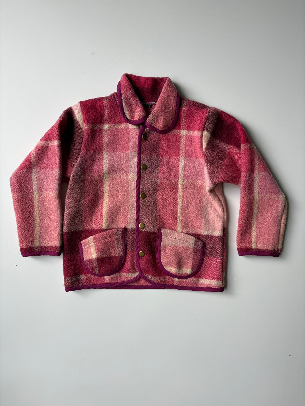 Pink and red plaid blanket children's jacket with a Peter Pan collar and front buttons, laid flat on a light gray background.