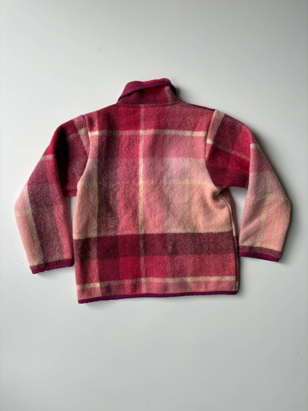 Pink and red plaid blanket children's jacket with a Peter Pan collar and front buttons, laid flat on a light gray background.