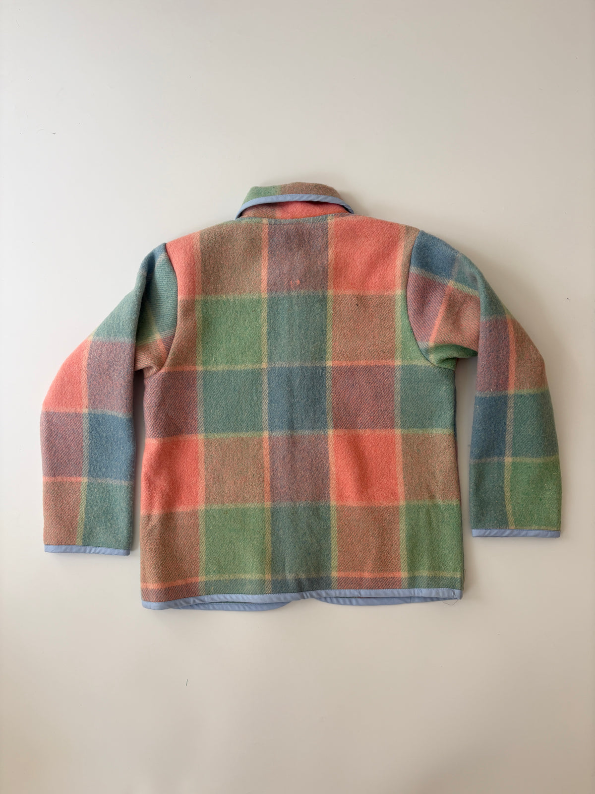 Pink green and blue blanket plaid children's jacket. A vintage-style plaid jacket with a pastel color scheme of green, pink, and blue, featuring a Peter Pan collar and front button closure, laid flat against a neutral background.