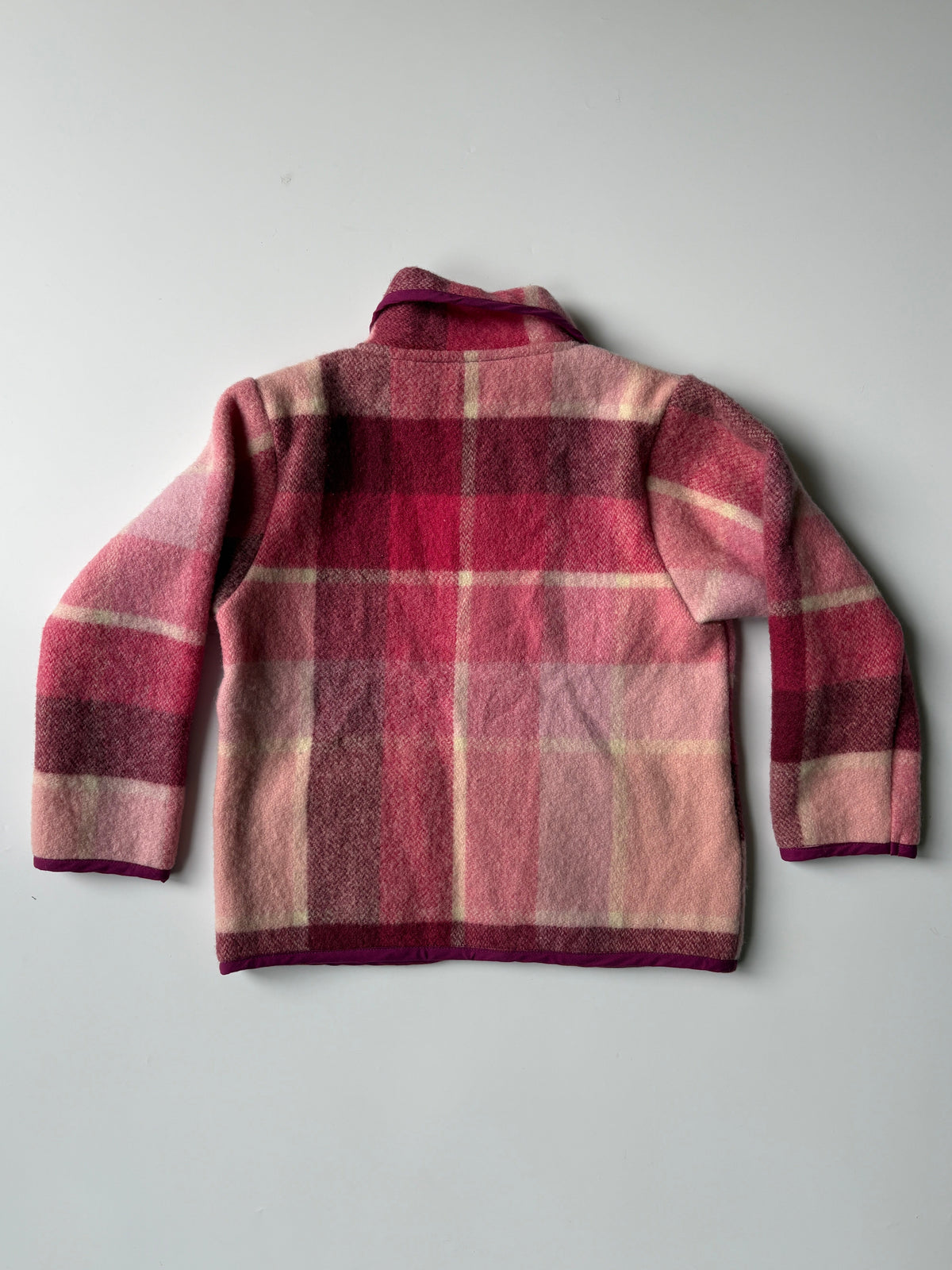 A pink and red plaid blanket children's jacket with a Peter Pan collar and front buttons, laid flat on a light gray background.