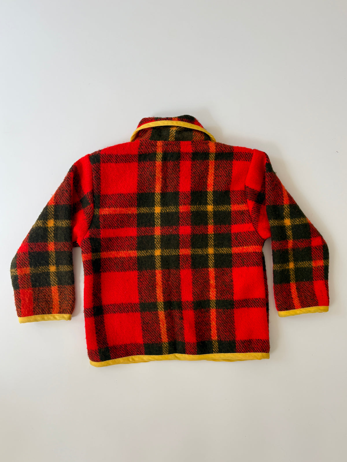 Red and black plaid blanket children's jacket. A red and black plaid children's jacket with yellow trim, featuring a Peter Pan collar, button closure, and front pockets, laid flat against a light background.