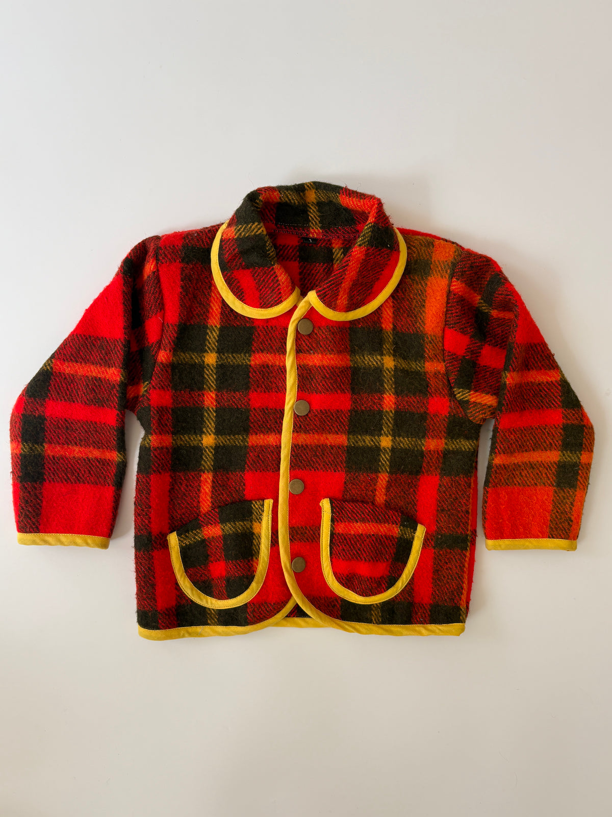 Red and black plaid blanket children's jacket. A red and black plaid children's jacket with yellow trim, featuring a Peter Pan collar, button closure, and front pockets, laid flat against a light background.
