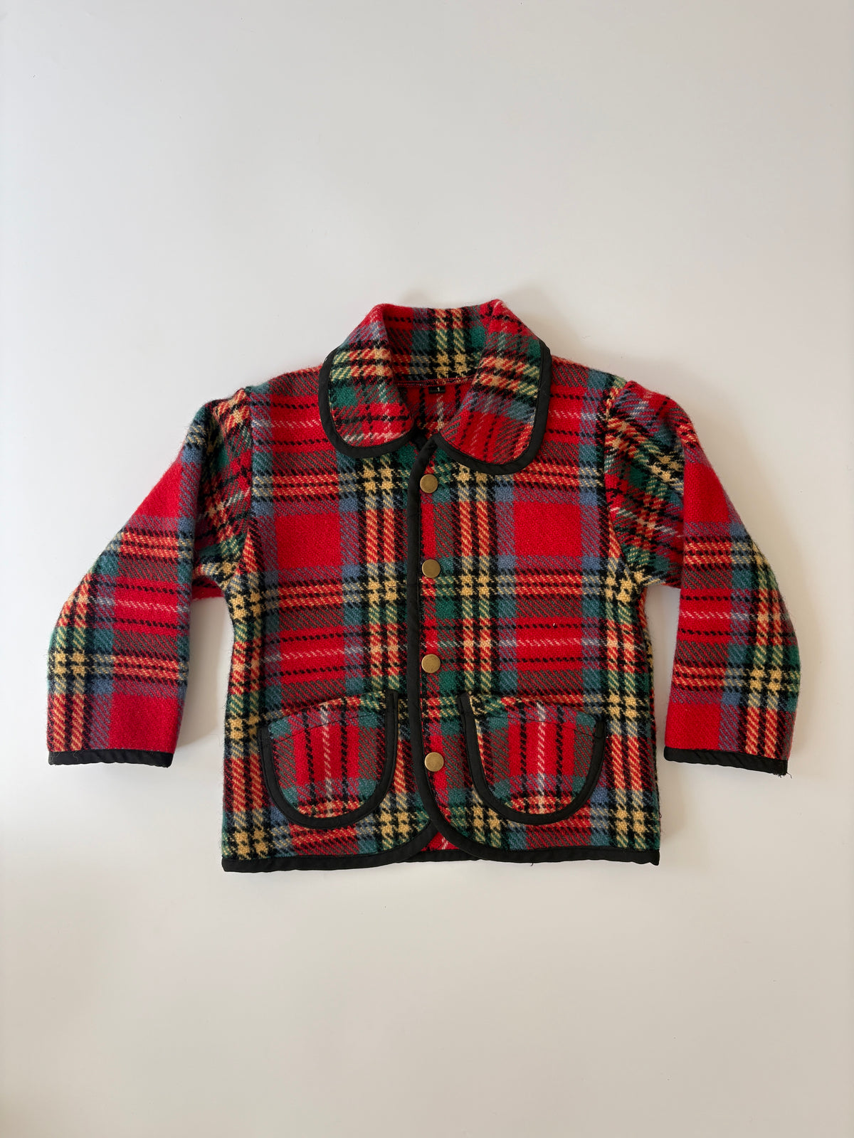 A red and green tartan plaid children's jacket with black trim, a collar, and front buttons, laid flat against a light background.