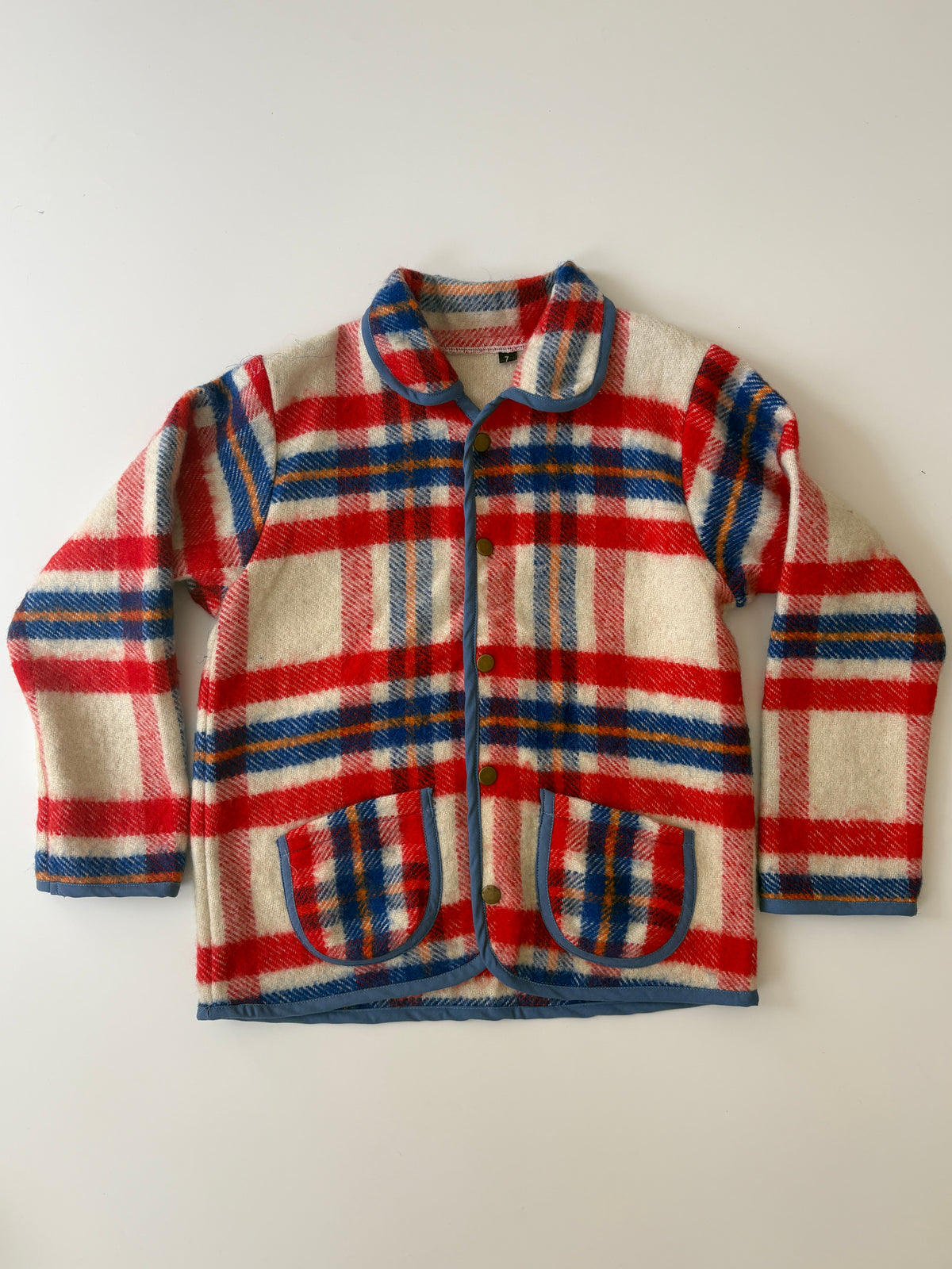 Red white & blue plaid blanket children's jacket. A vintage plaid wool jacket with red, blue, and cream stripes, featuring a button-up front and two front patch pockets, laid flat on a light background.