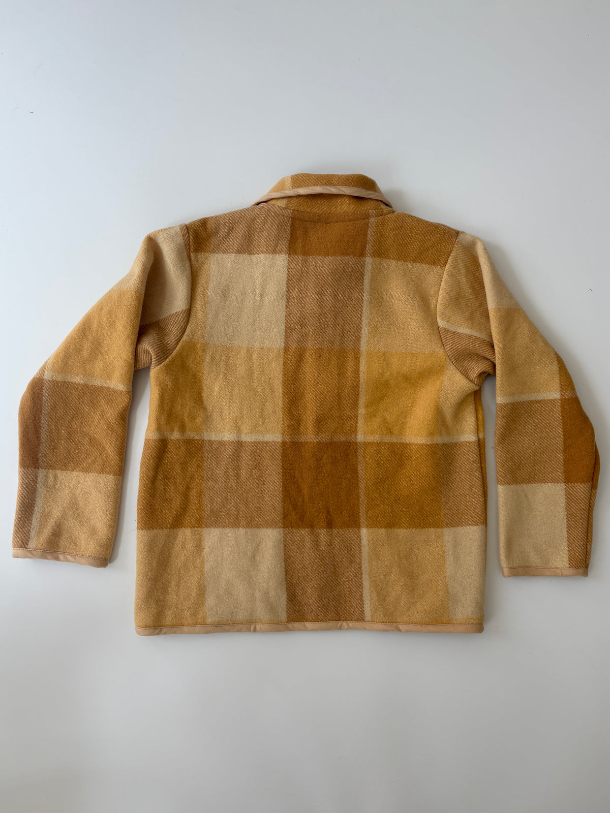 Tan and Brown plaid children's blanket jacket. A children's long-sleeve button-front jacket in a warm tan and brown plaid fabric, featuring a collar, dark buttons, and two front patch pockets, laid flat on a light gray background.
