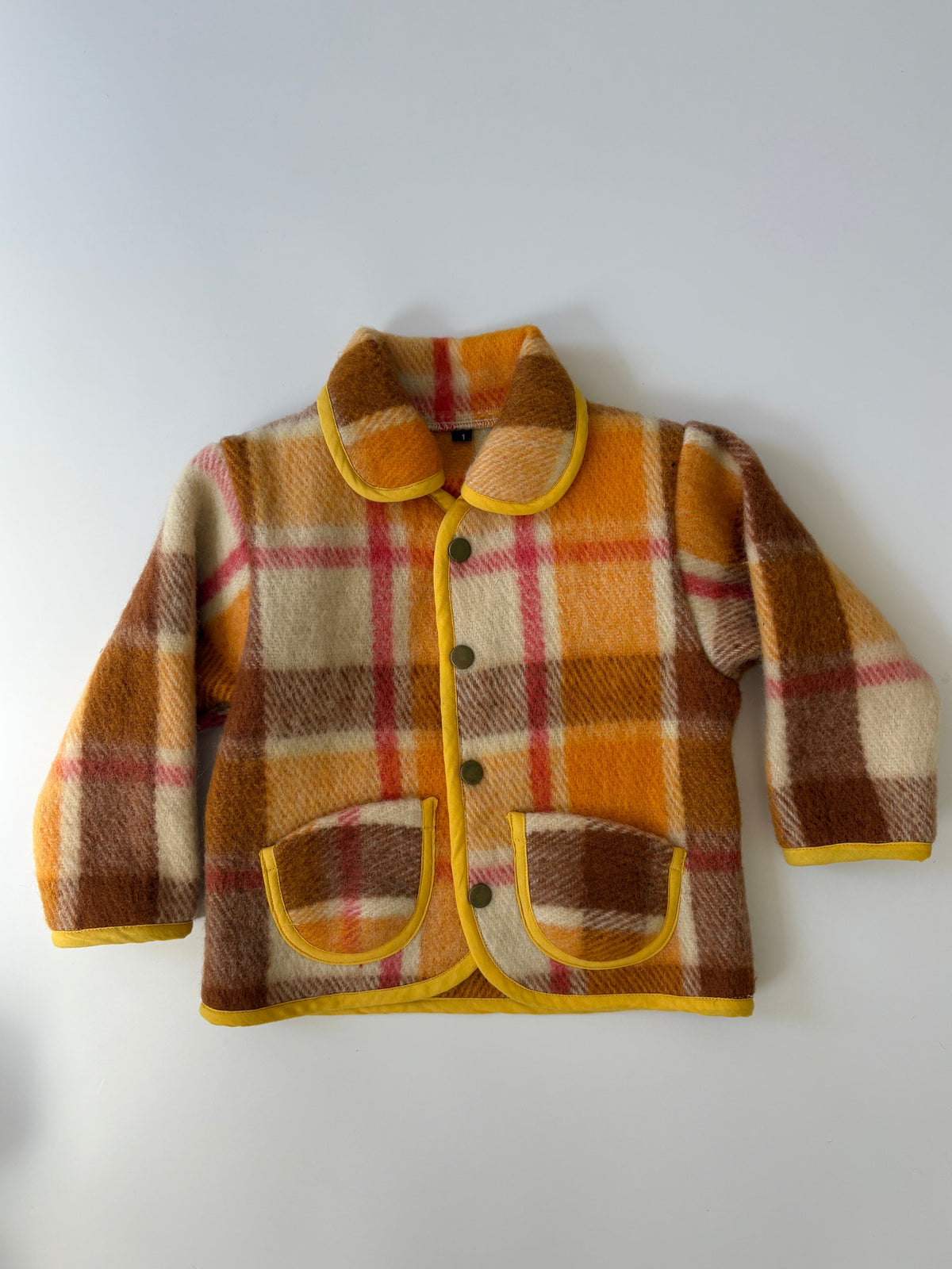 Upcycled children's plaid jacket in orange, brown, and cream, featuring a yellow collar, trim, and pocket edges, laid flat against a light gray background.
