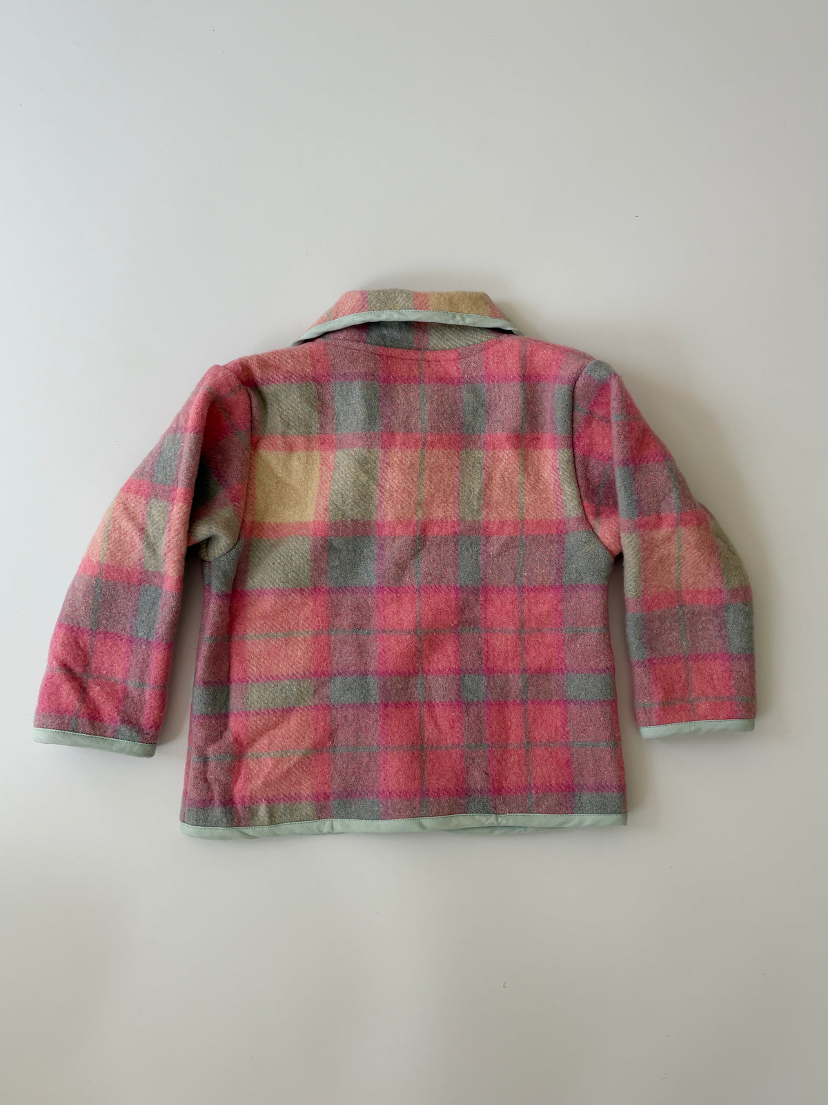 An upcycled children's plaid jacket in pink, red, and gray wool, featuring a Peter Pan collar and pocket trim, laid flat against a neutral off-white background.