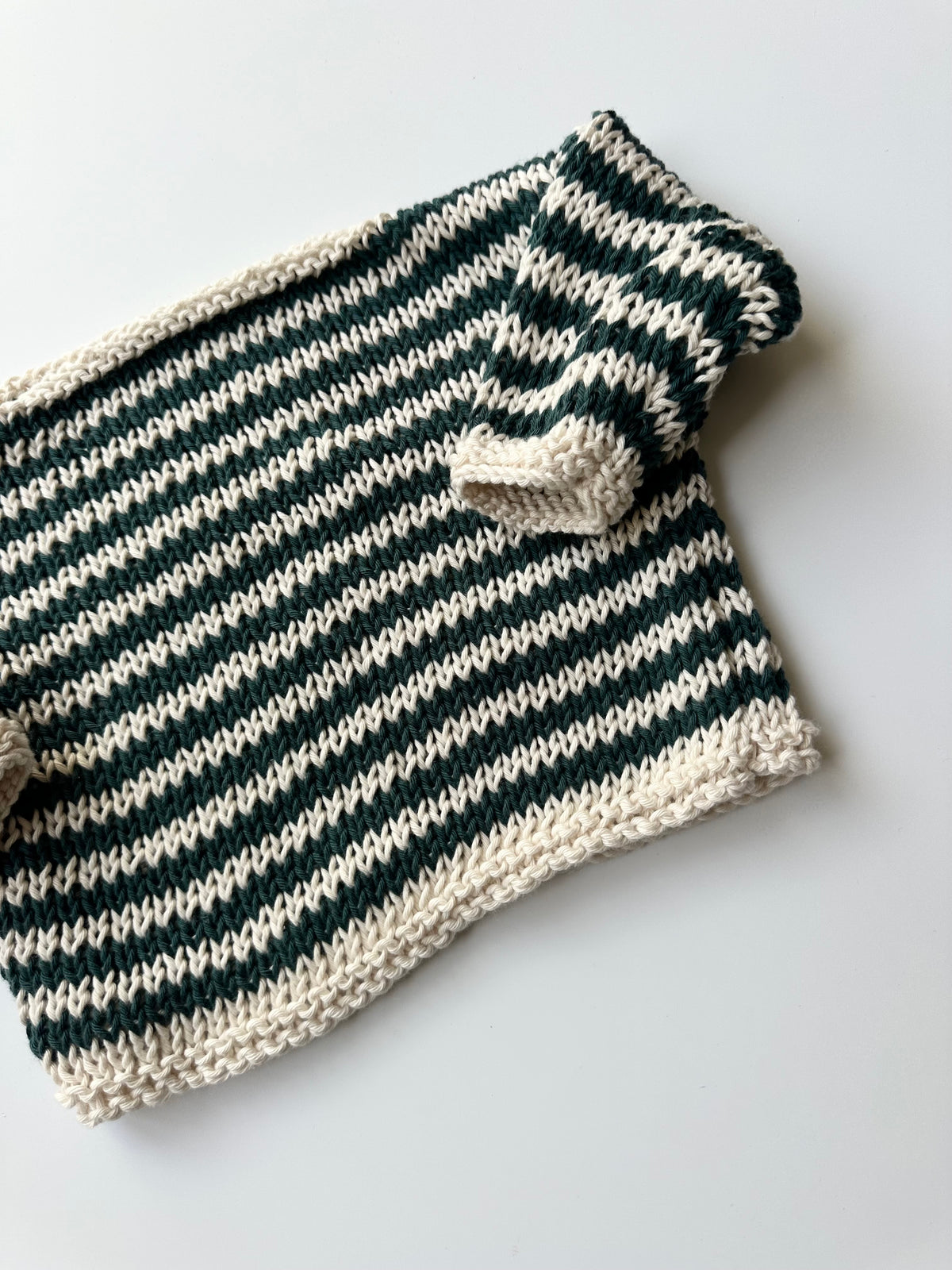 Close up of a hand-knit children's jumper in alternating blue and white colors, laid flat on a light gray background.