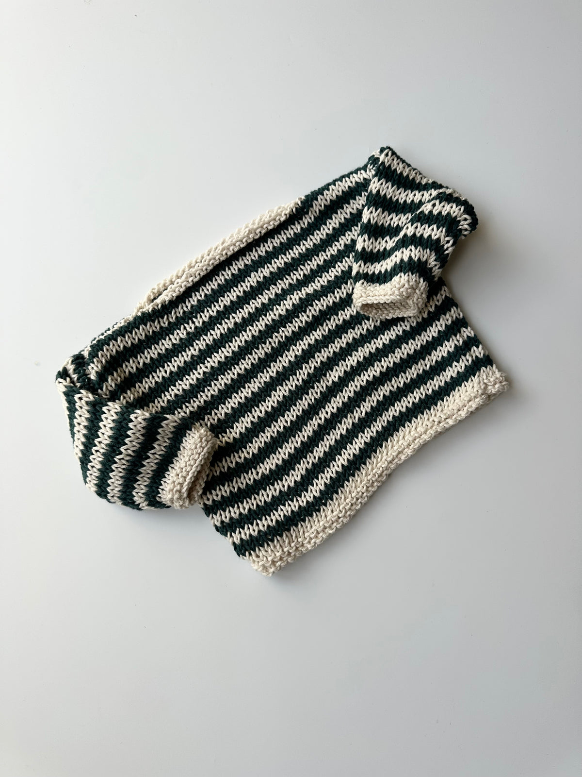 A hand-knit children's jumper in alternating blue and white colors, laid flat on a light gray background.
