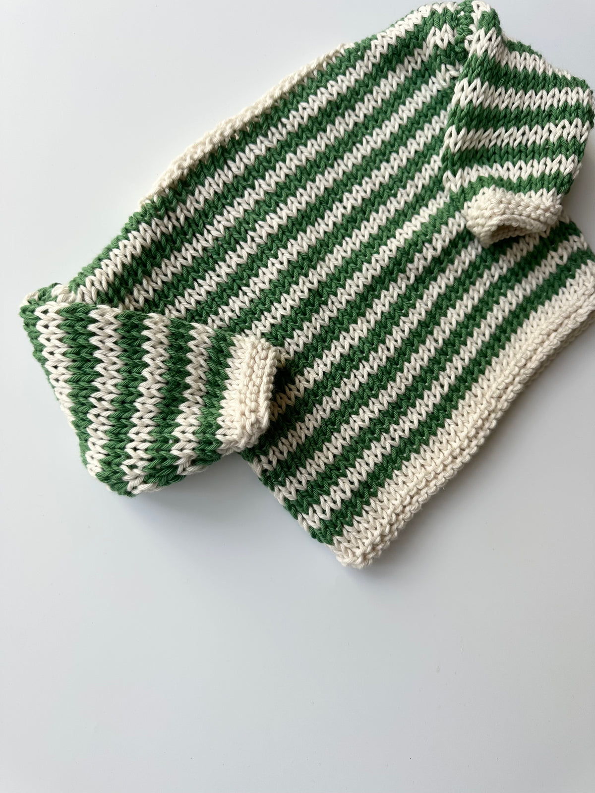 A hand-knit striped sweater in green and cream, lying flat on a light gray background.